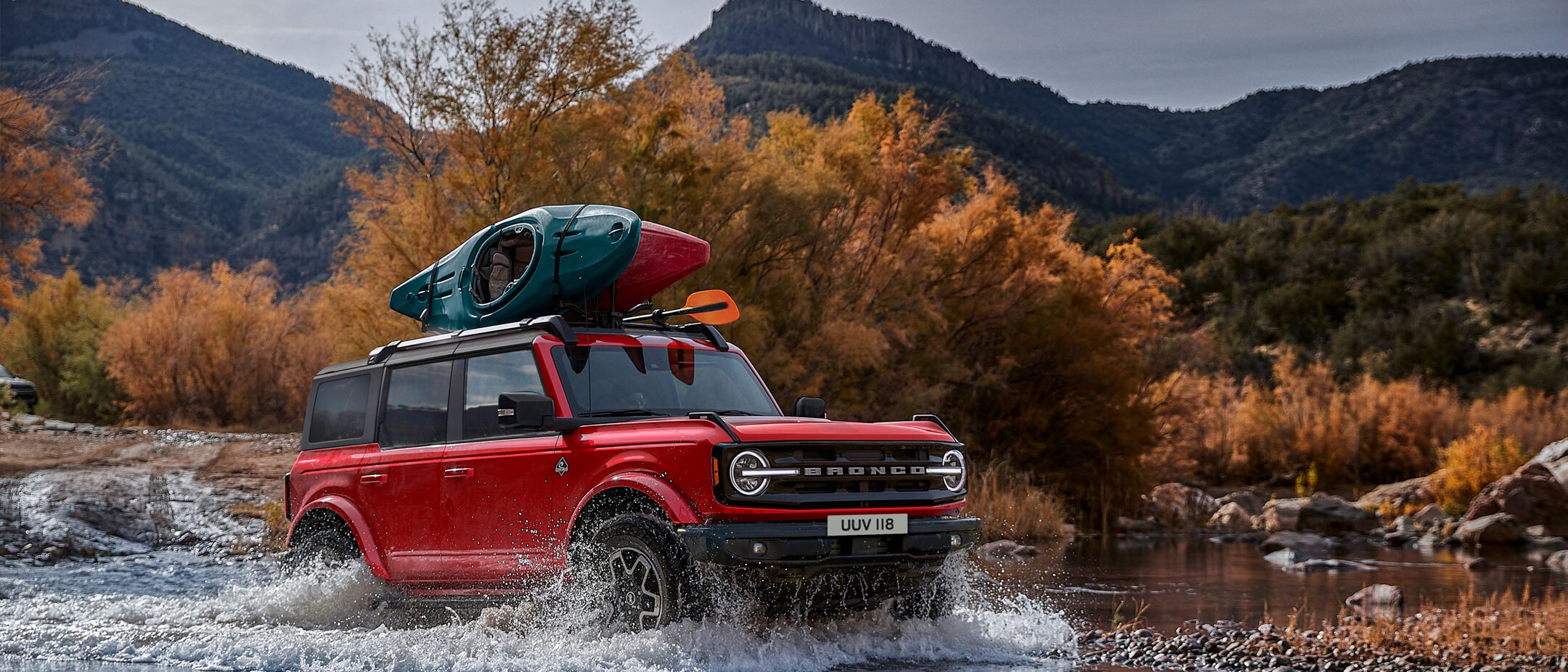 Ford Bronco in Rot. Dreiviertel-Frontansicht, in den Bergen durch einen Fluss fahrend.