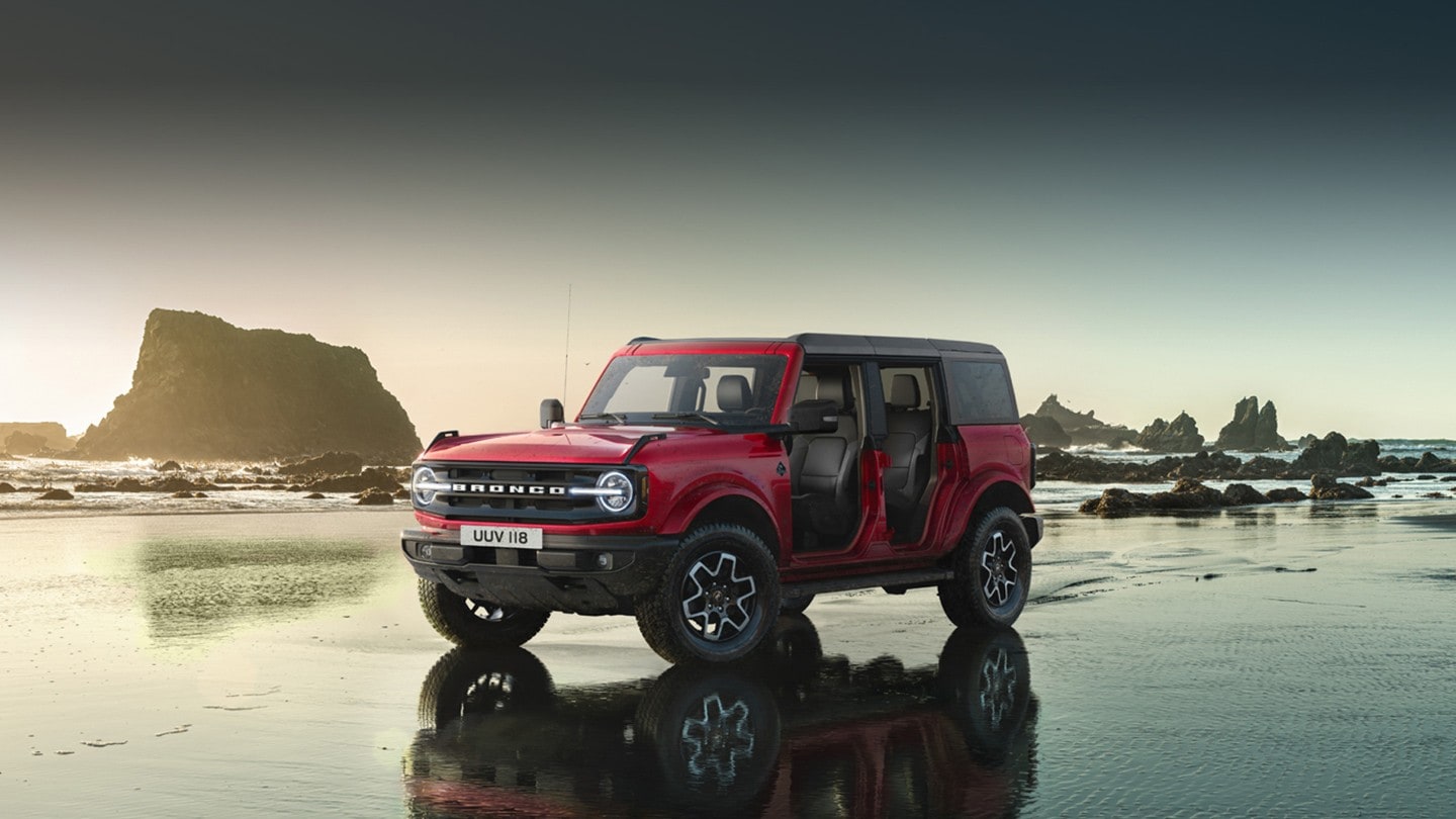 Ford Bronco in Rot. Dreiviertel-Frontansicht, in den Bergen durch einen Fluss fahrend.