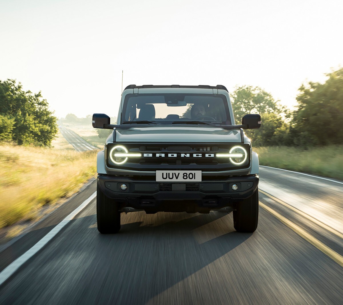 Ford Bronco in Grau. Frontansicht, auf einer Landstrasse fahrend.