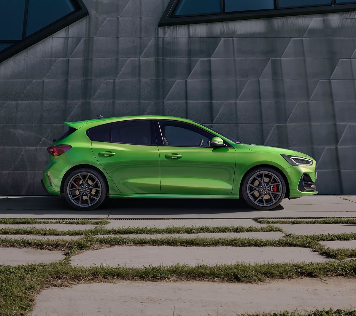 Ford Focus ST in Grün. Seitenansicht, vor einer grauen Wand stehend.