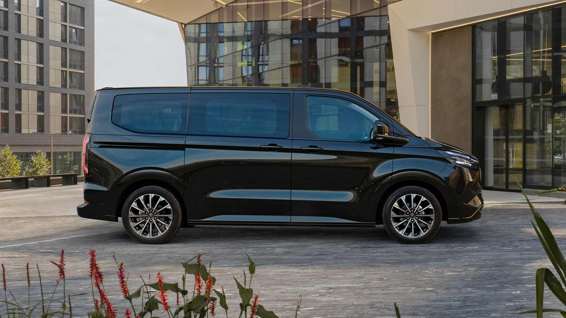 Schwarzer Ford E-Tourneo Custom vor modernem Gebäude geparkt