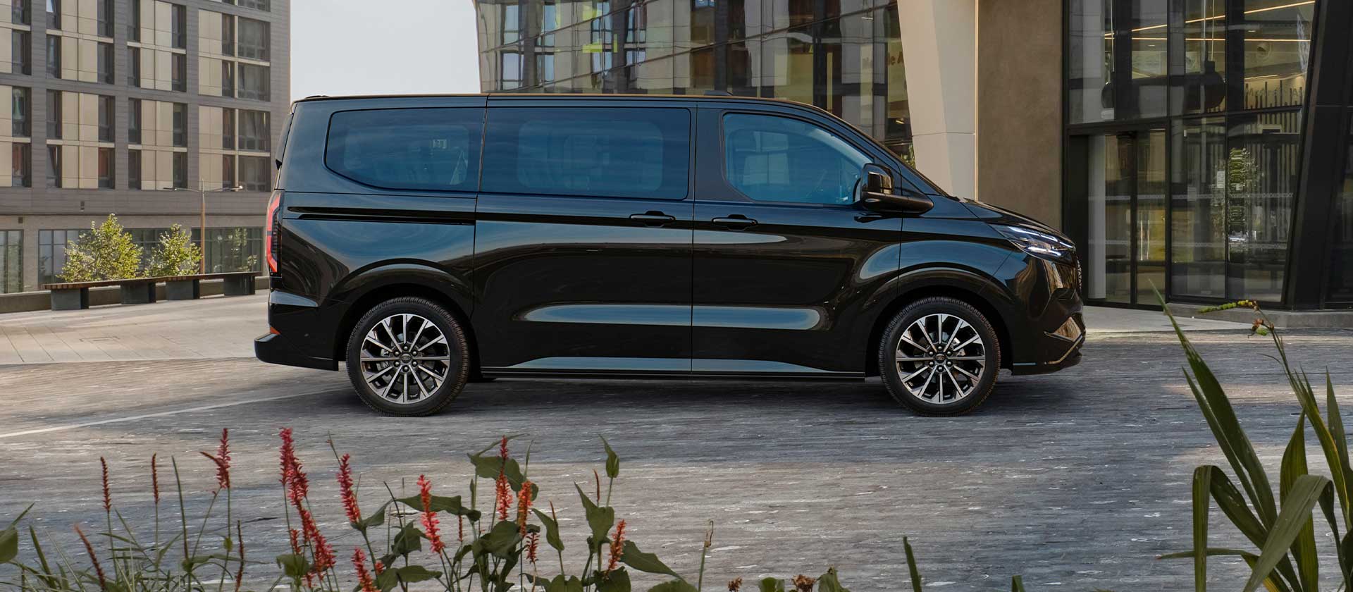 Schwarzer Ford E-Tourneo Custom vor modernem Gebäude geparkt