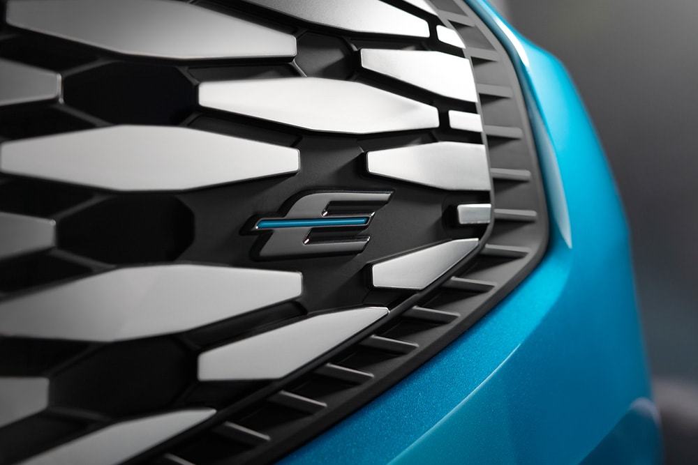 Nahaufnahme des Ford E-Tourneo Custom Kühlergrills mit blauem \E\" Logo, exklusiv für Ford Elektrofahrzeuge"