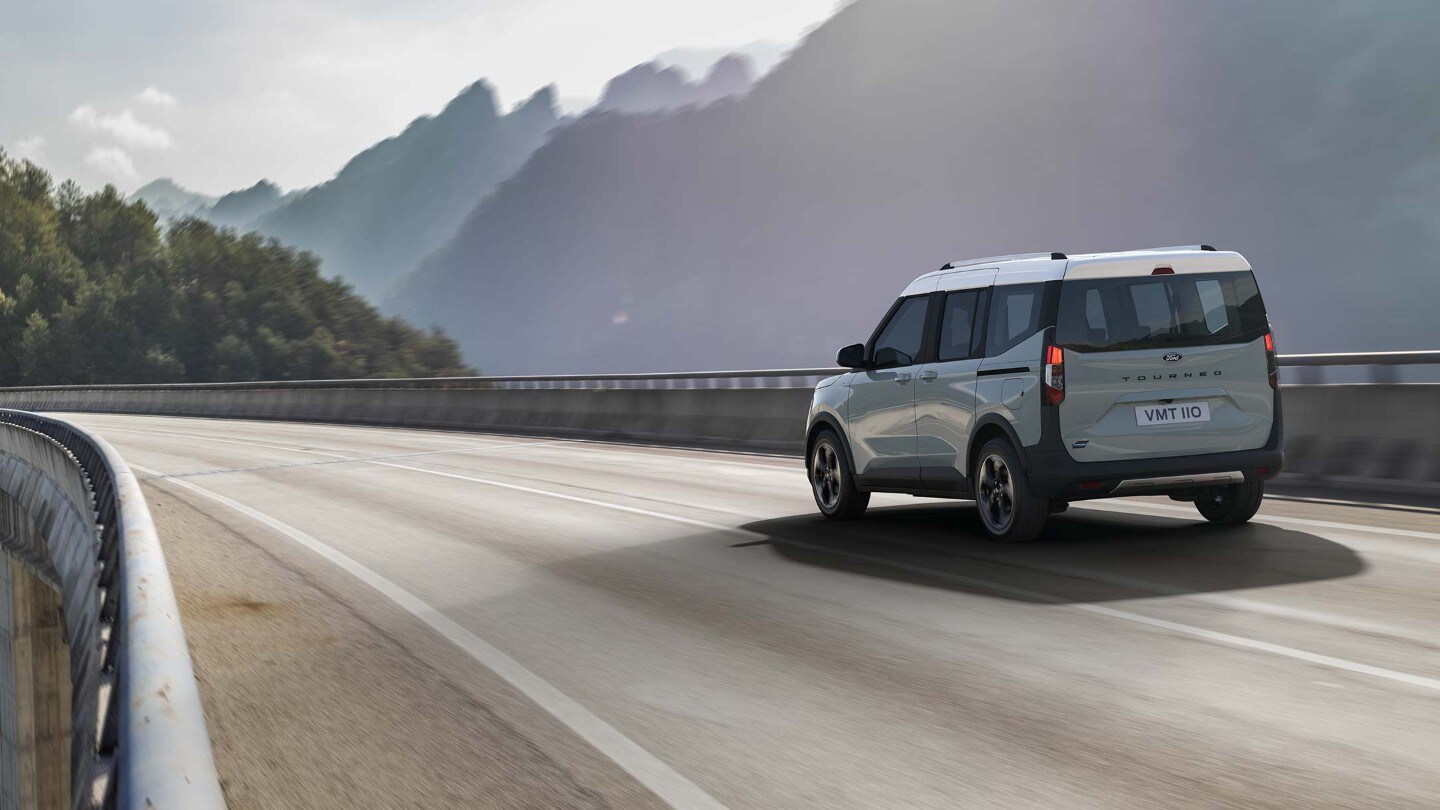 Ford Tourneo Courier in Grau in der ¾ Heckansicht fährt über eine Brücke