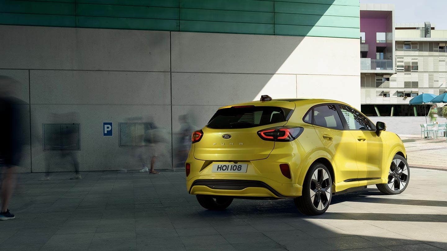 Heckansicht eines vollelektrischen Ford Puma Gen-E in Gelb®, der unter einer Brücke parkiert ist.