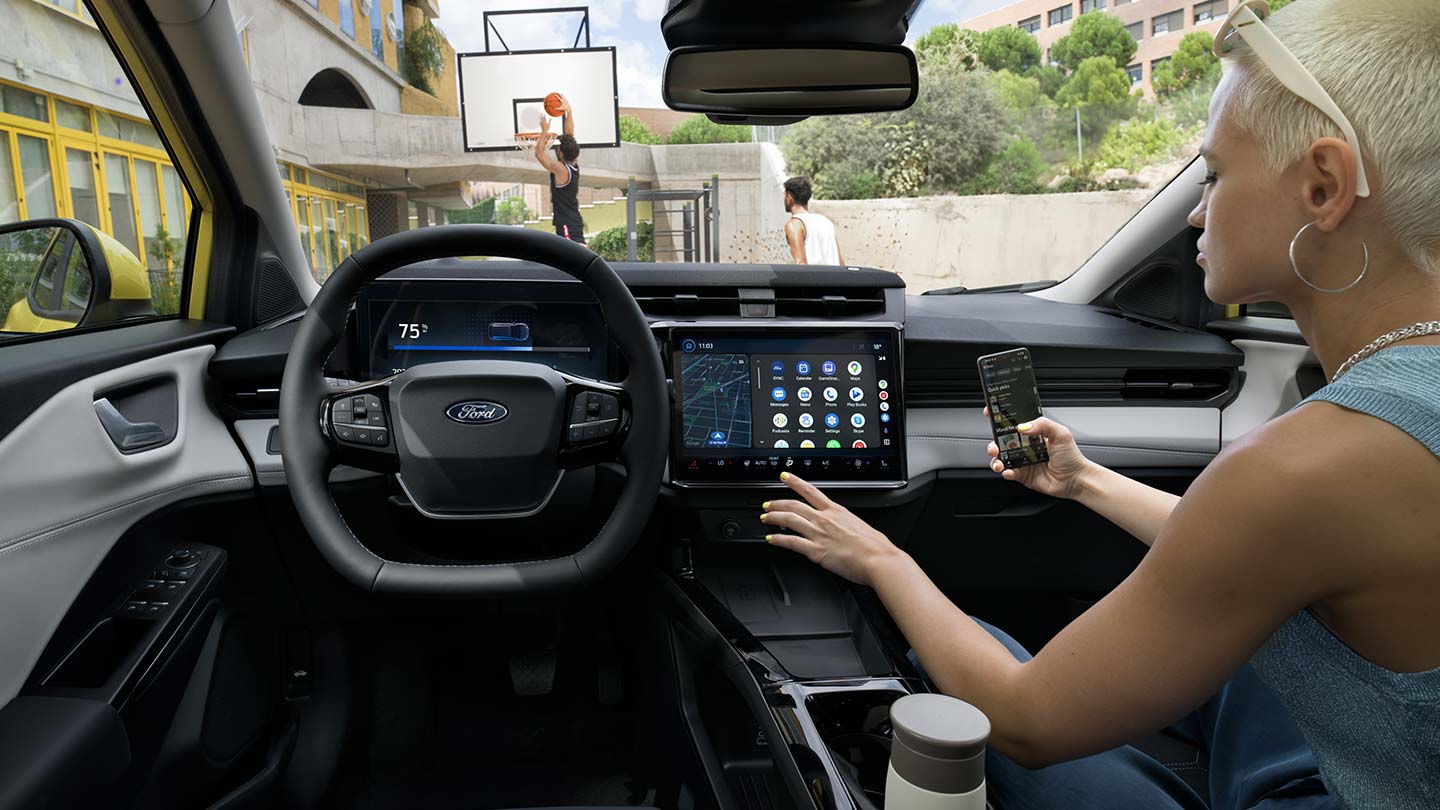 Innenraum des vollelektrischen Ford Puma Gen-E ®, während eine Person ein Mobiltelefon kabellos mit dem Touchscreen synchronisiert.