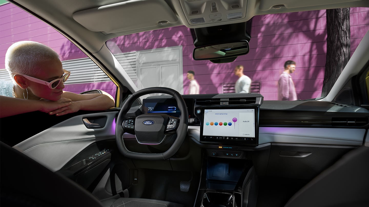 Person, die durch das offene Fenster der Fahrertür in den Innenraum des vollelektrischen Ford Puma Gen-E® schaut und sich den grossen Touchscreen und die Innenraumbeleuchtung ansieht.