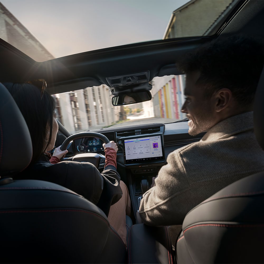 Fahrer und Beifahrer unterhalten sich während der Fahrt durch eine sonnige Landschaft.