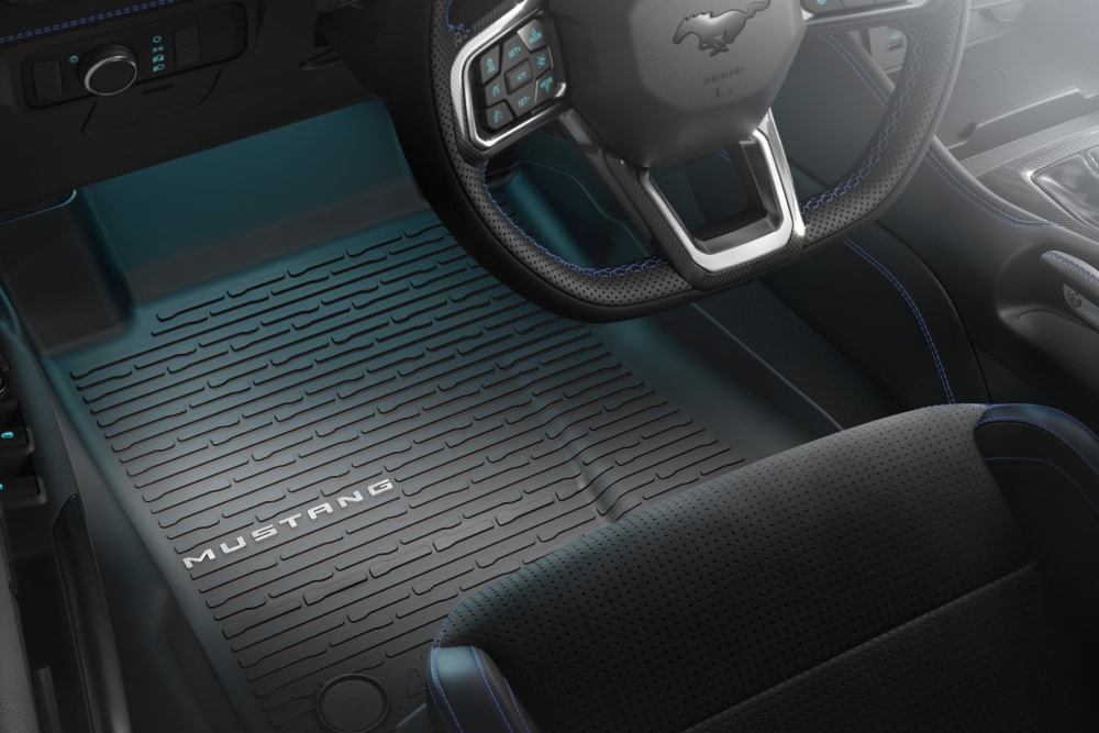 Innenansicht eines Ford Mustang mit Blick auf das Lenkrad und eine Allwetterfussmatte mit Muster und Schriftzug.