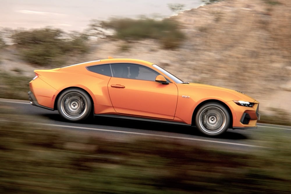 Seitenansicht des Ford Mustang GT Fastback in Orange Fury, der eine Straße entlangfährt