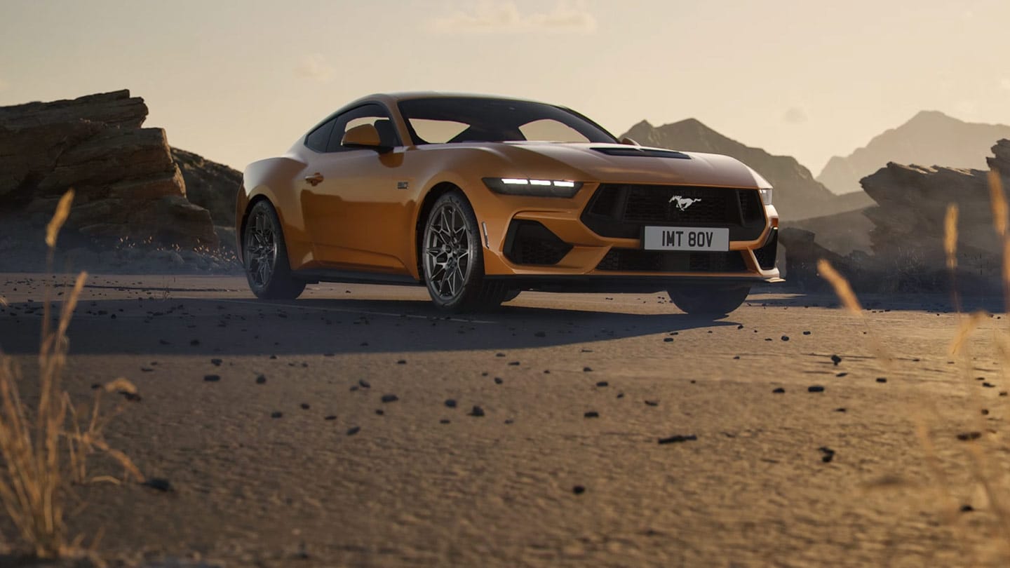 Seitenansicht eines orangefarbenen Ford Mustang, der in einer felsigen Wüstenlandschaft geparkt ist. 