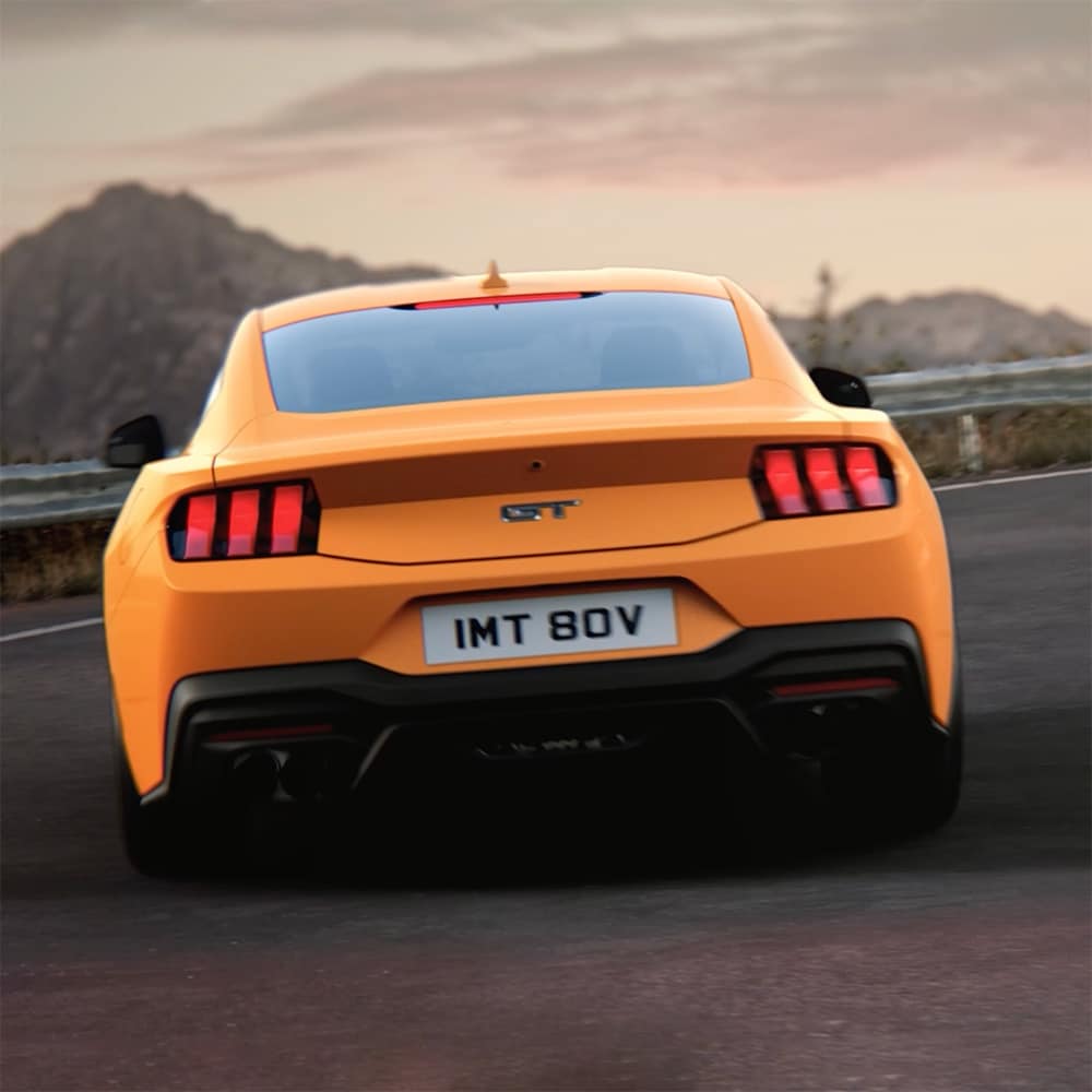 Das Heck eines Ford Mustang GT Fastback in Orange Fury, der eine enge Kurve auf einer Landstraße fährt