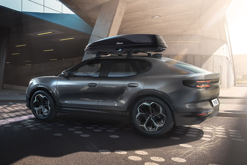 Seitliche 3/4-Ansicht eines roten Ford Capri mit Dachbox, geparkt unter einer modernen Gebäudestruktur.