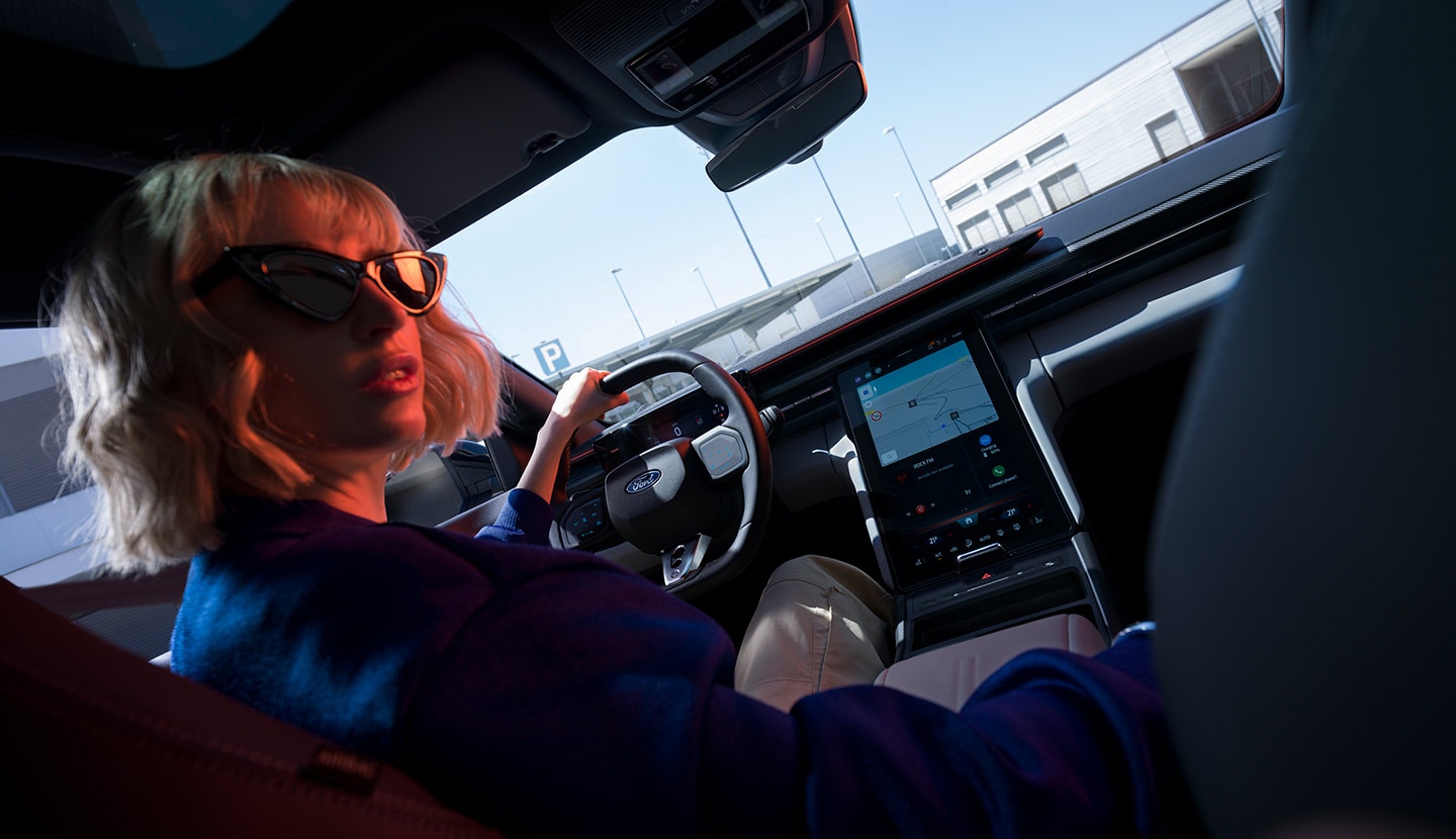 Eine Frau sitzt auf dem Fahrersitz eines geparkten Ford Capri®, wobei das Lenkrad und der grosse SYNC® Move-Touchscreen sichtbar sind.