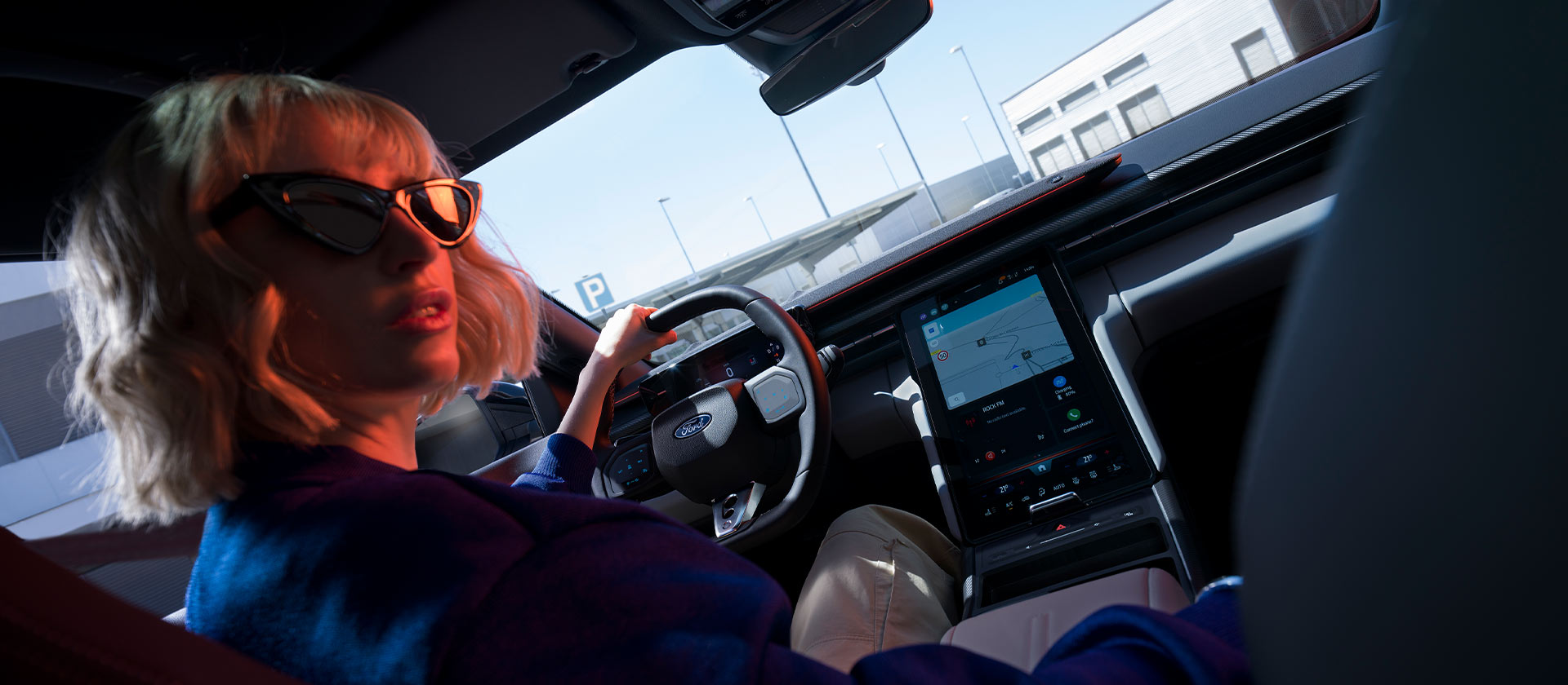 Eine Frau sitzt auf dem Fahrersitz eines geparkten Ford Capri®, wobei das Lenkrad und der grosse SYNC® Move-Touchscreen sichtbar sind.