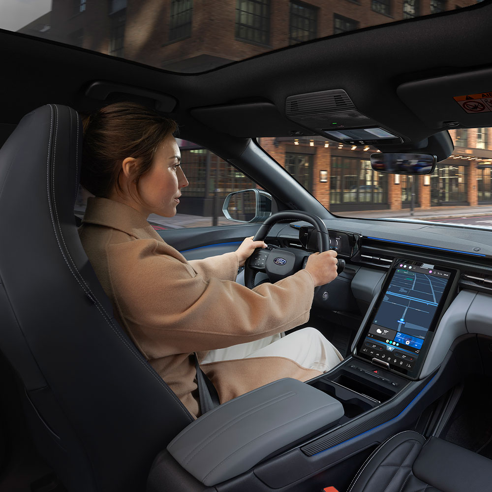 Eine Person, die den elektrischen Ford Explorer durch die Stadt fährt, zeigt den großen 14,6" SYNC Move Touchscreen.