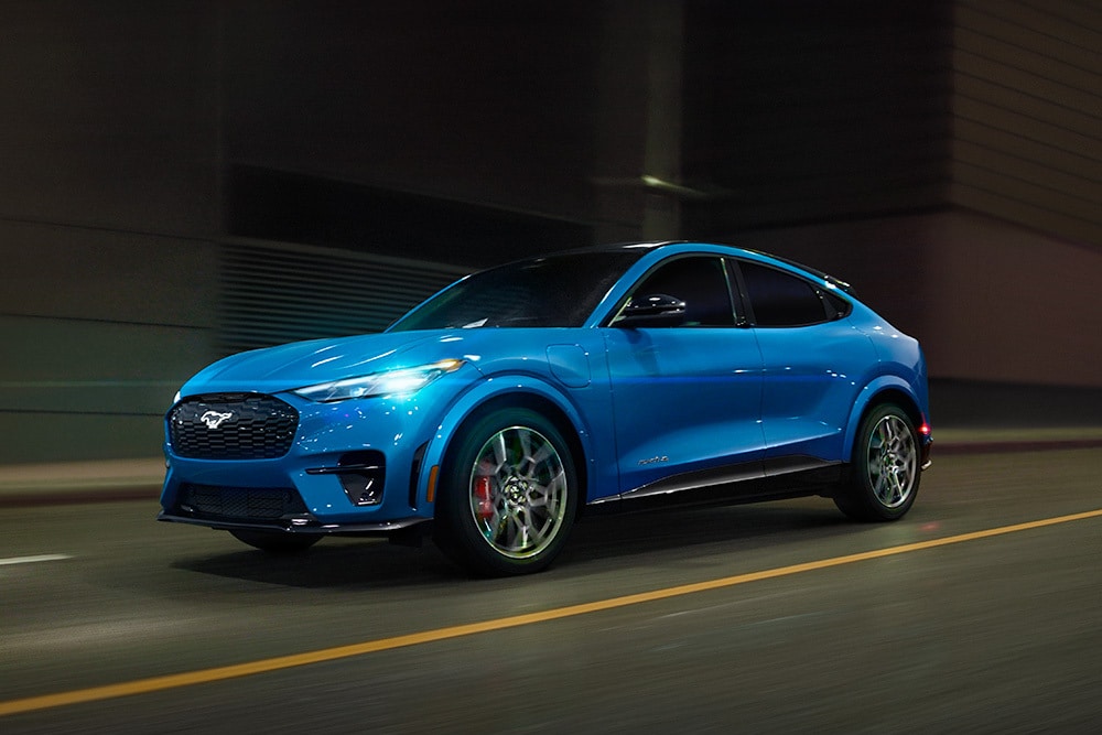 Ein blauer Elektro-Sportwagen des Modells Ford Mustang Mach-E GT fährt auf offener Strasse.