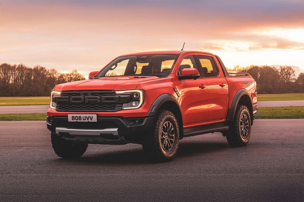 Ein orangefarbener Pick-up-Truck des Modells Ford Ranger Raptor steht inmitten einer malerischen Landschaft.