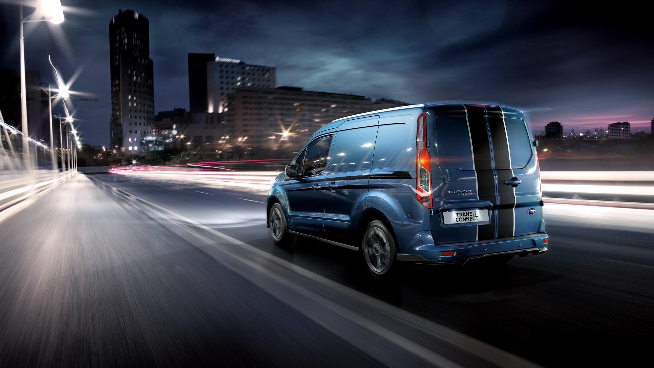 Ford Transit Connect in Blau ¾-Heckansicht fährt bei Nacht durch Grossstadt 