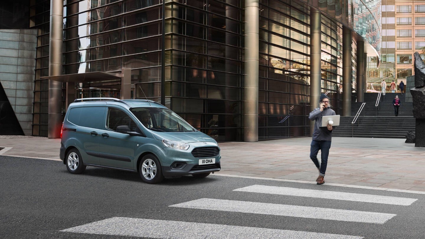 Ford Transit Courier in Grau Seitenansicht hält vor Zebrastreifen in der Innenstadt