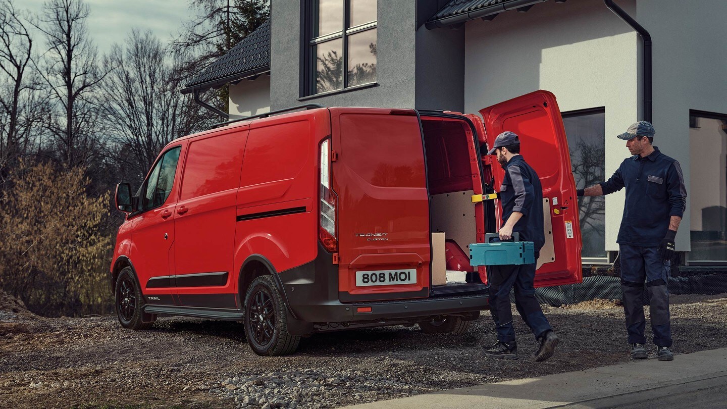 Ford Transit Custom Trail Rot ¾-Heckansicht parkt in Neubaugebiet und wird beladen