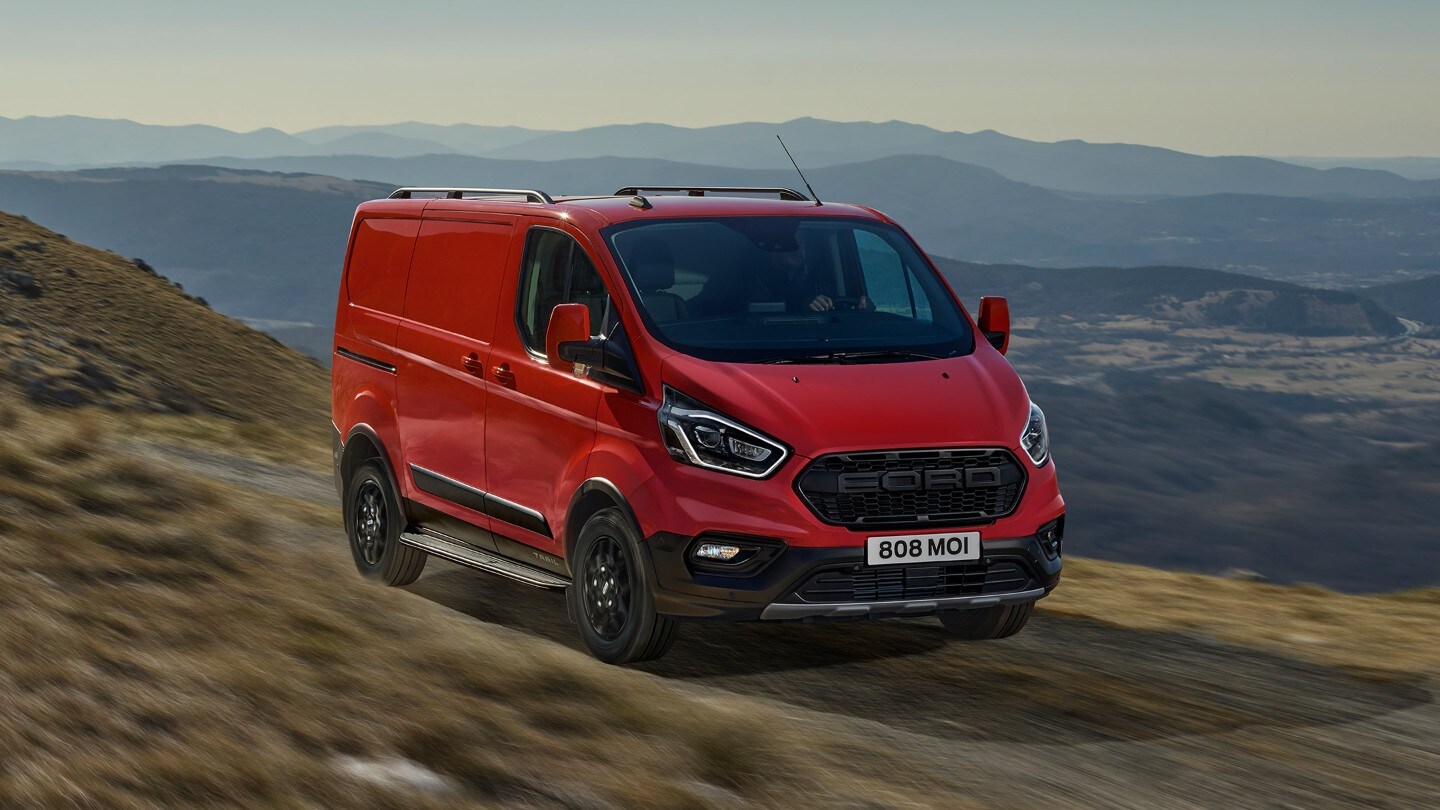Ford Transit Custom Kastenwagen Trail Rot ¾-Frontansicht fährt auf Feldweg im Gebirge