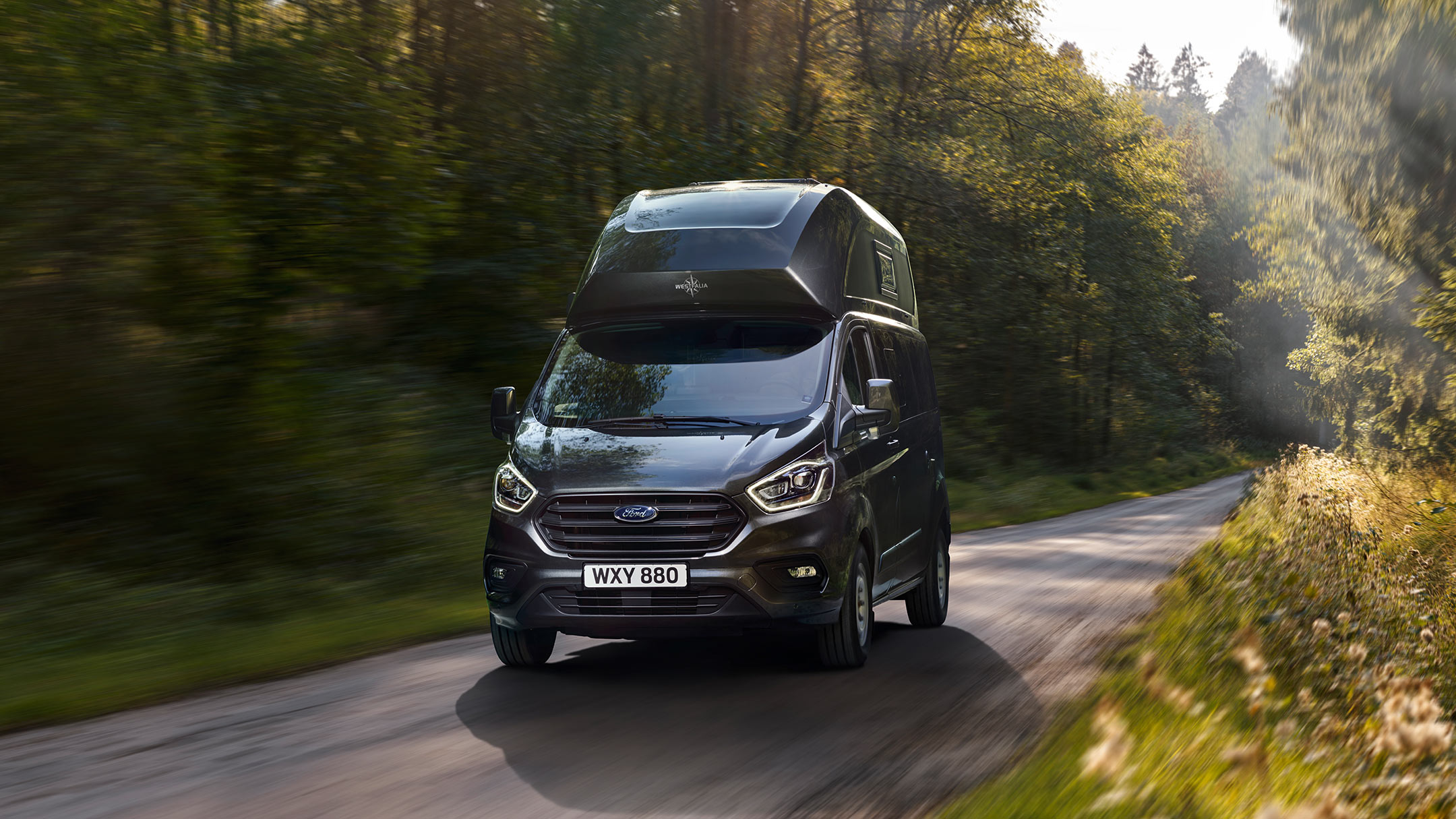 New Grey Ford Transit Custom Nugget Plus front view driving in forest