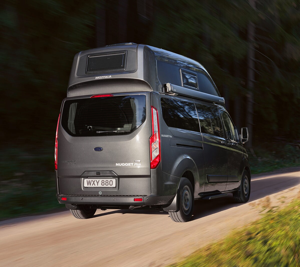 New Grey Ford Transit Custom Nugget rear view driving in forest
