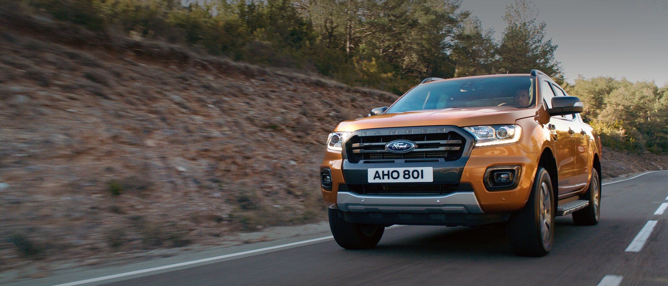 Ford Ranger Orange ¾-Frontansicht in Bewegung auf kurvenreicher Straße durch Wald 