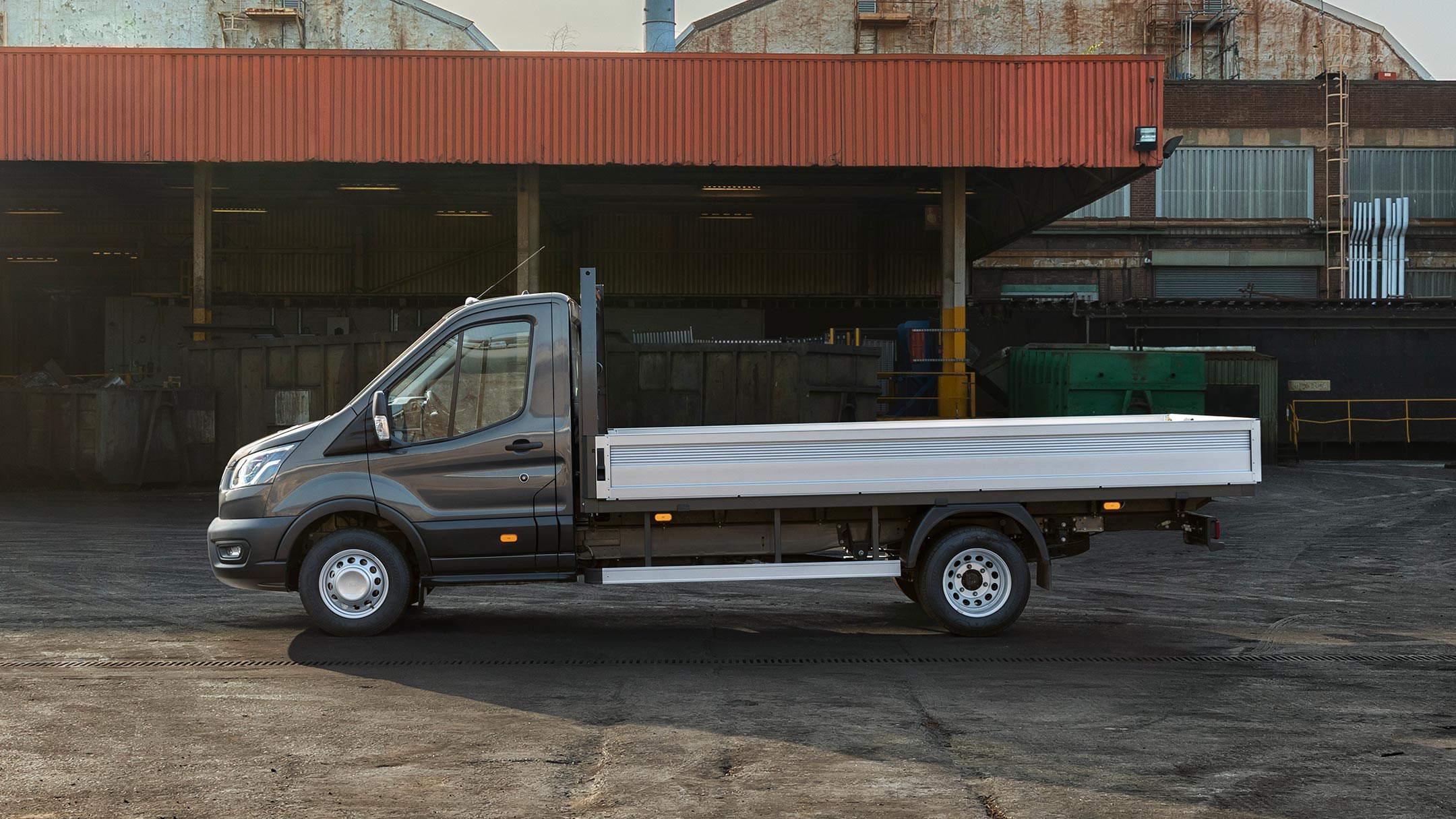 Ford Transit 5 Tonnen Fahrgestell schwarz Seitenansicht parkt auf Betriebsgelände neben Überdachung mit Paletten