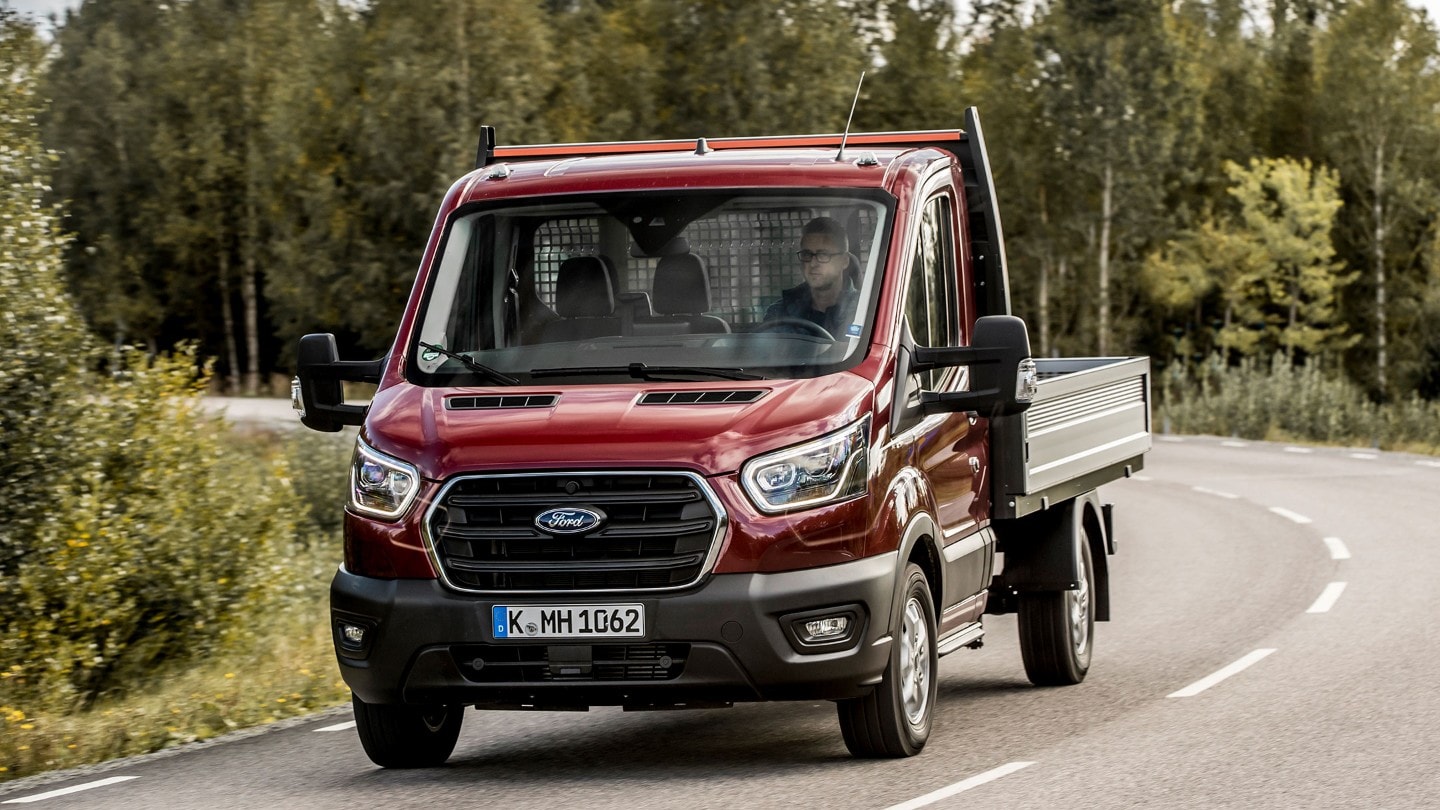 Ford Transit Fahrgestell in Rot ¾ Frontansicht auf Landstrasse fahrend