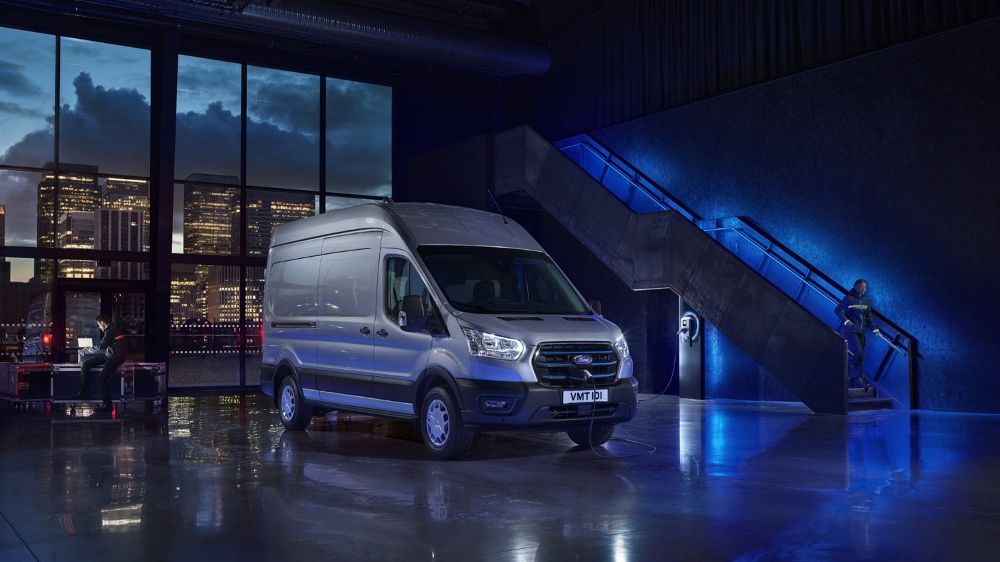 Ford E-Transit silber ¾-Frontansicht parkt in Lagerhalle mit blauer Ambientebeleuchtung