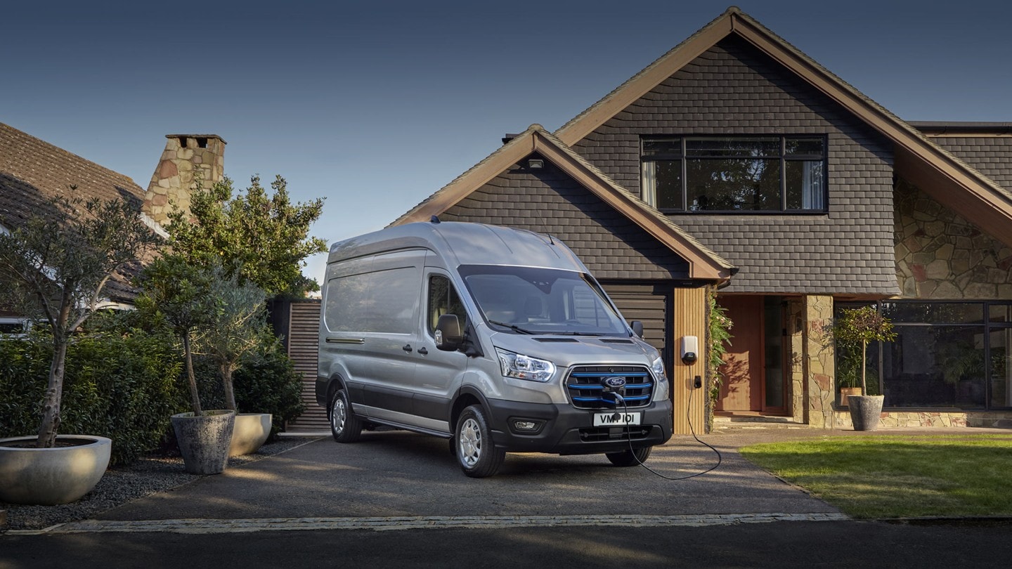 Ford E-Transit silber ¾-Frontansicht parkt vor Wohnhaus und wird aufgeladen