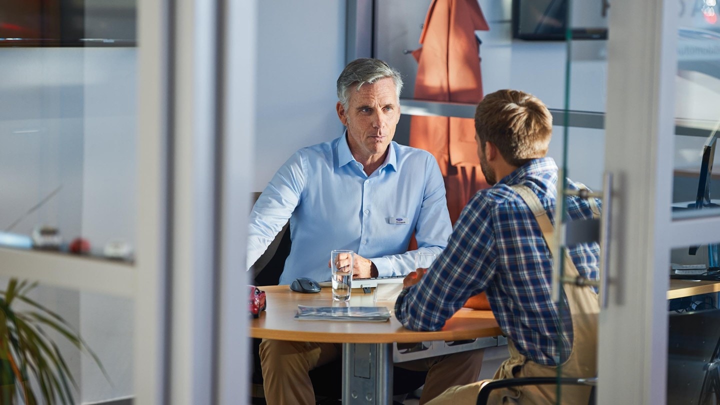 Zwei Männer sitzen sich an Büroschreibtisch gegenüber 