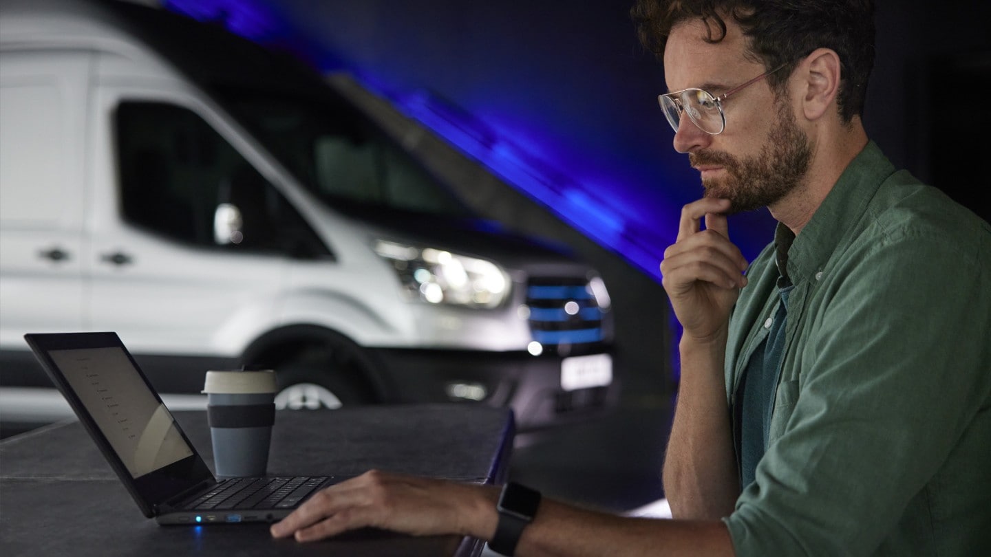 Mann sitzt am Laptop mit Ford E-Transit Ausschnitt im Hintergrund