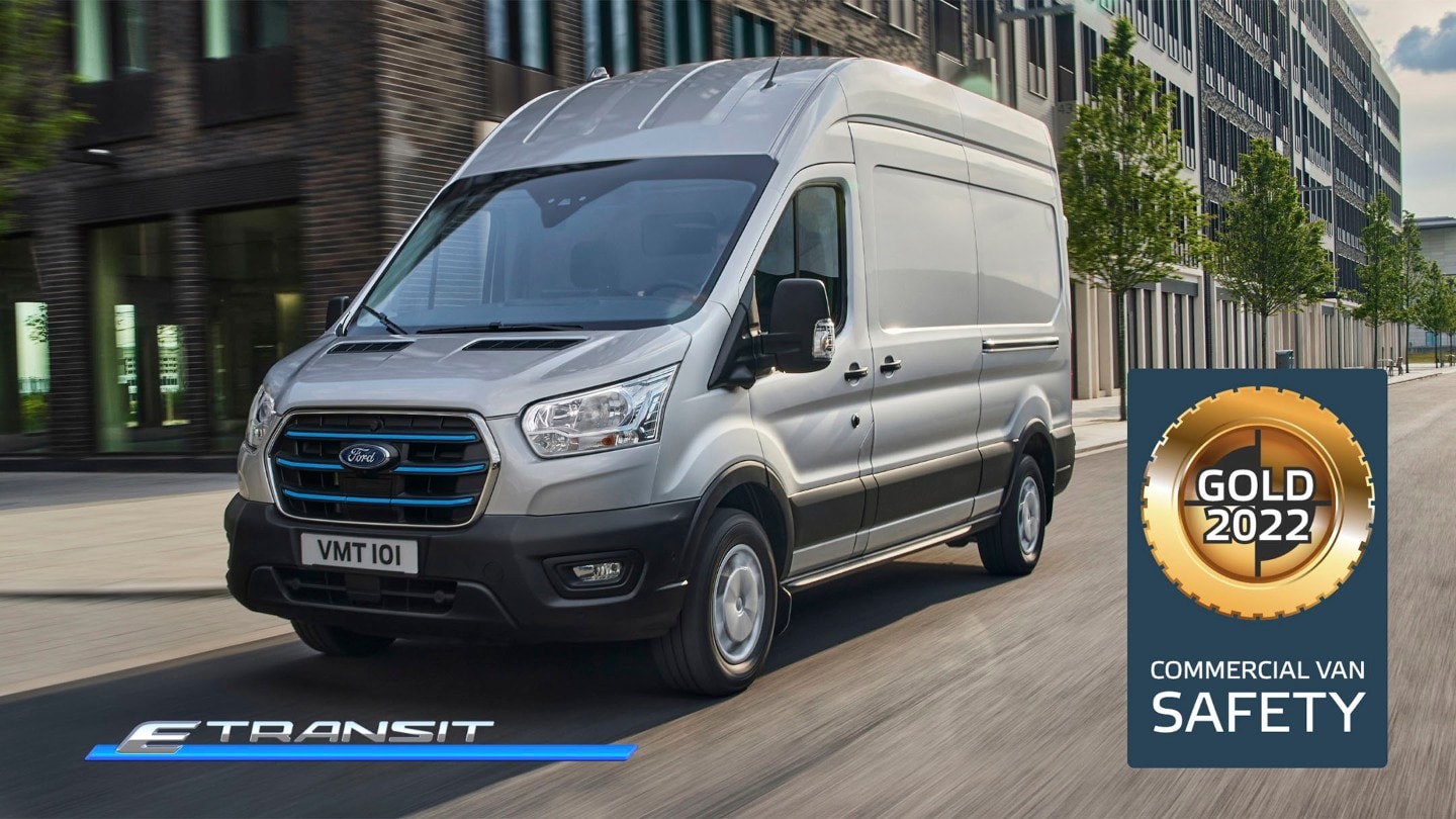 Ford E-Transit Kastenwagen in Silber ¾-Seitenansicht fährt entland Hochhäuser und NCAP Gold-Log für Kategorie „Sicherheit“