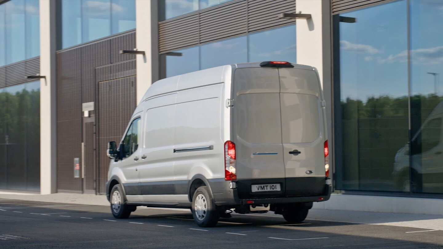 Ford E-Transit in Silber ¾-Heckansucht parkt vor modernem Gebäude