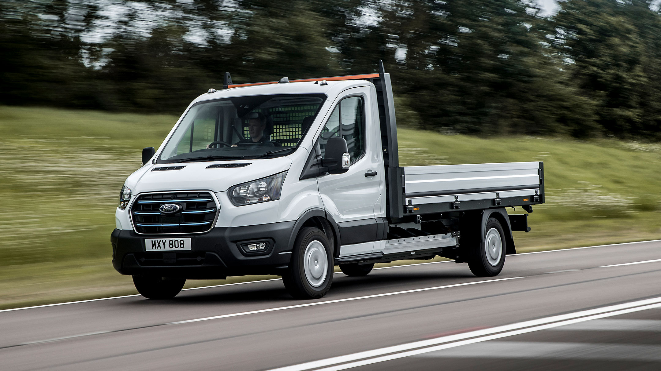 Ford E-Transit Fahrgestell in Weiss in der ¾-Frontansicht auf einer Landstrasse fahrend