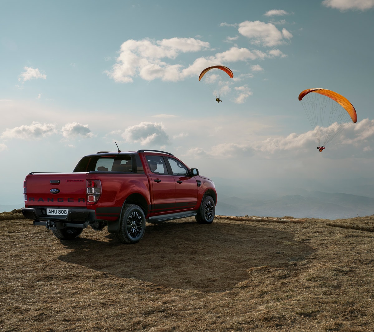 Ford Ranger Stormtrak rot ¾-Seitenansicht parkt in Dünenlandschaft und Paraglider am Himmel