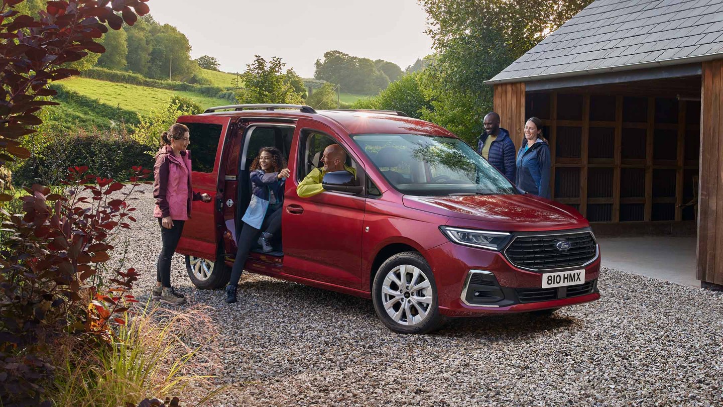 Ford Grand Tourneo Connect in Rot ¾-Frontansicht parkt auf Kiesweg vor Wohnhaus