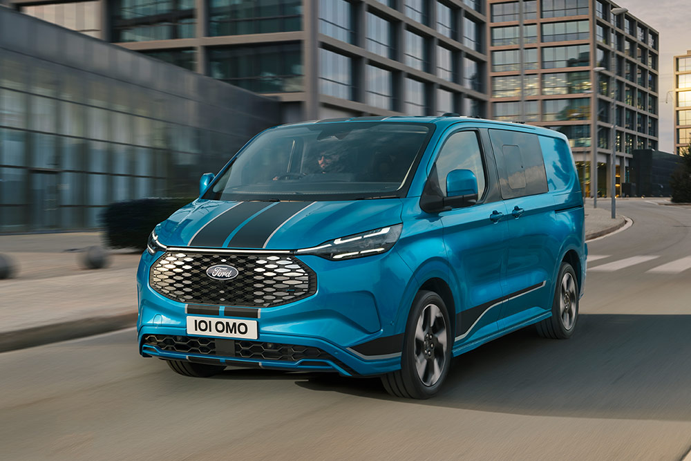 Blauer Ford E-Transit Custom Sport Doppelkabine Transporter fährt auf einer Stadtstrasse.