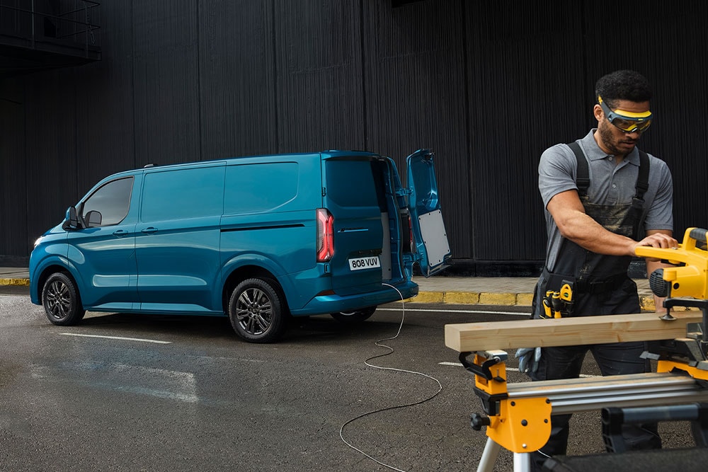 Blauer Ford E-Transit Custom Elektro-Transporter und Person mit Elektrowerkzeug.