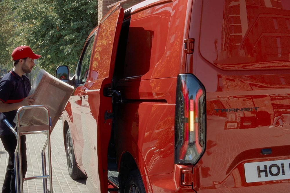 Auslieferer entlädt Pakete aus rotem Ford E-Transit Custom. 