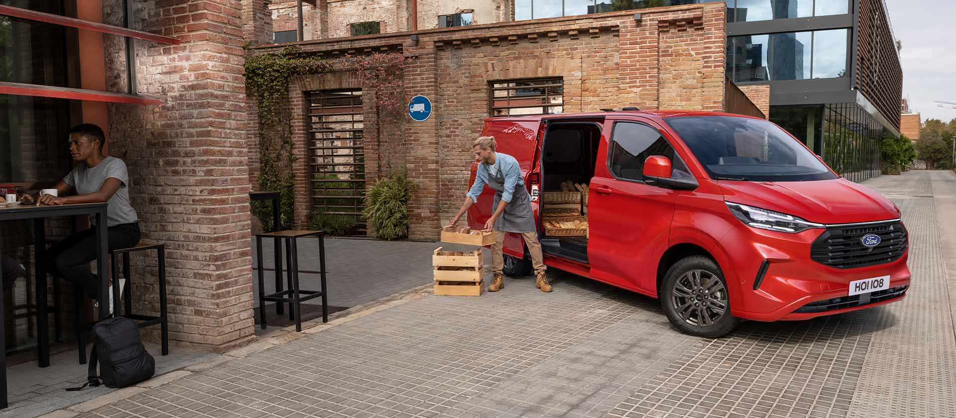 Roter Ford Transit Custom Transporter geparkt vor einem Cafe.
