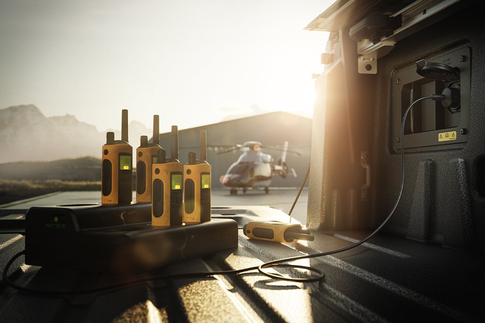 Mehrere Walkie-Talkies, die bei Sonnenuntergang auf der Ladefläche eines Ranger Raptors aufgeladen werden, in der Ferne ein Helikopter.