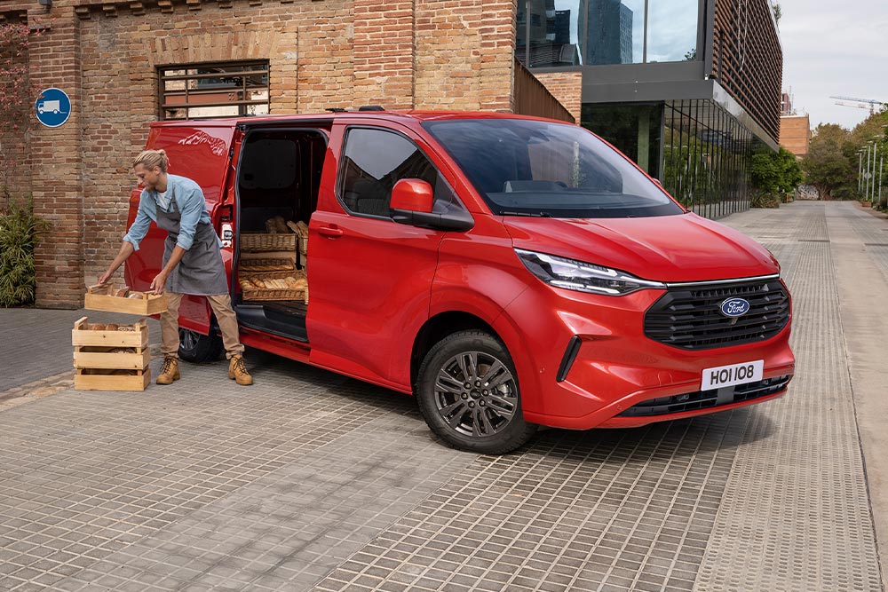 Zusteller lädt Pakete in einen roten Ford Transit Custom