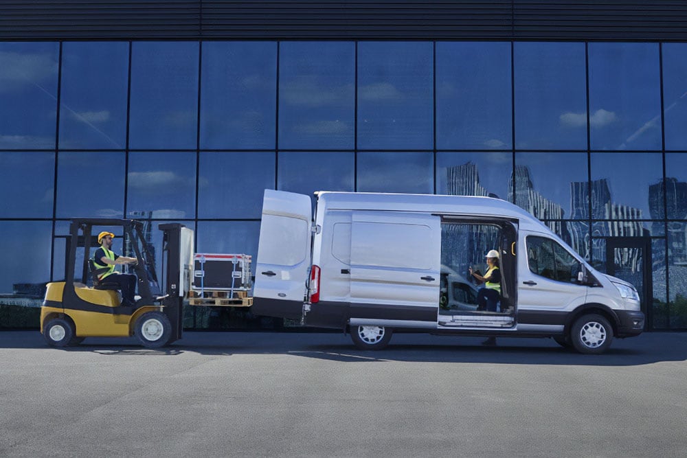 Zwei Personen laden mit einem Gabelstapler Fracht in einen silbernen Ford Transit Van.