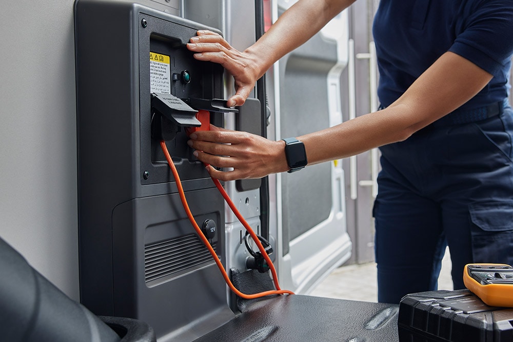 Nahaufnahme einer Person, die ein Ladekabel an einen Ford  E-Transit Elektro-Van  anschliesst.