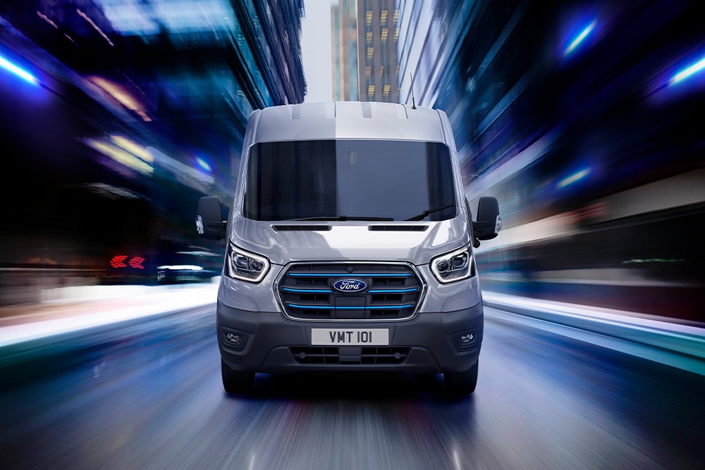 Dunkelgrauer Ford E-Transit Elektro-Van, der auf einer Strasse fährt.