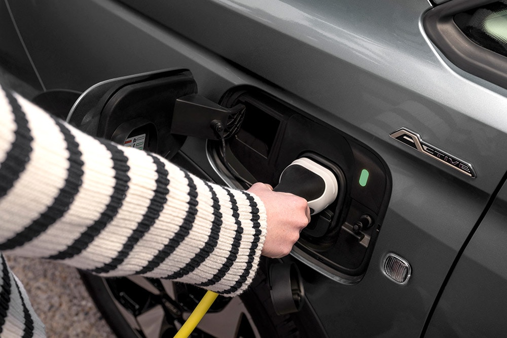 Eine Person, die ein Ladekabel an einen Ford Transit Connect  Plug-in-Hybrid anschliesst.